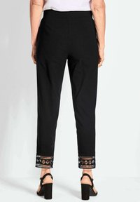 Zwarte broek met een gestructureerde zoom en geometrische patronen. Ontworpen in een getailleerde pasvorm met een gladde afwerking en een taps toelopend been.