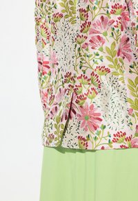 Blusa floreale con fiori rosa e foglie verdi su uno sfondo chiaro, abbinata a una gonna verde pastello.