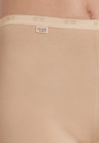 Beige högmidjade trosor gjorda av mjukt tyg, med ett dekorativt elastiskt midjeband med ett subtilt mönster och en liten logotagg.