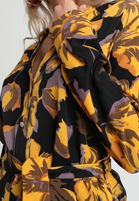 Blommönstrad klänning med stora gula, lila och svarta blommor, med knäppning fram, flödande ärmar och midjebälte.