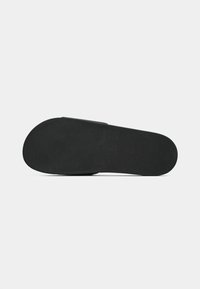 Black rubber sandal sole with textured grip and branded logo. Features a smooth, flat design and rounded shape for comfort.