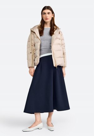 Beige puffer jacket with a zip closure, gray fitted sweater, and navy A-line skirt, complemented by white low-heeled shoes.