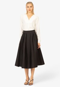 Blouse blanche avec un décolleté en V et des manches longues associée à une jupe plissée noire midi. Portée avec des sandales noires à lanières.