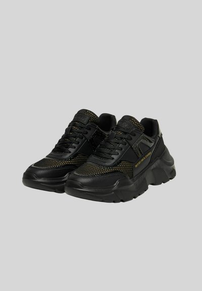 Sneakers neri con dettagli in rete e suola spessa. Presentano lacci neri, accenti testurizzati e logo dorato sul lato.