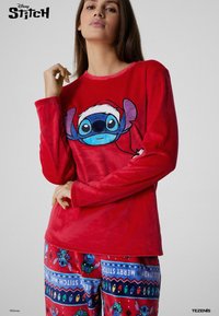 Camiseta larga de manga roja con un personaje de dibujos animados que lleva un gorro de Papá Noel. Combinada con pantalones de pijama estampados en colores rojo, azul y verde.