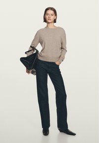 Maglione a maglia marrone chiaro, jeans dritti neri e borsa nera. I jeans hanno un taglio classico e la borsa presenta un design triangolare elegante.