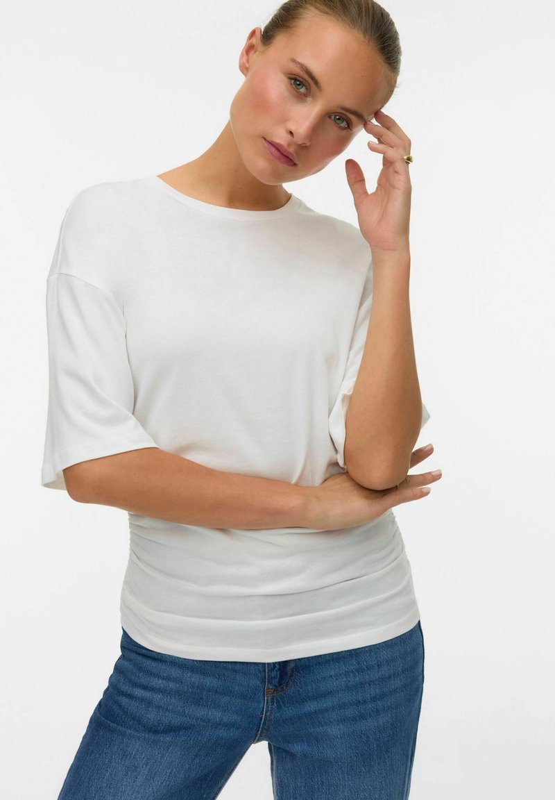 T-shirt blanche ample à manches courtes, texture douce, encolure ronde, associée à un jean en denim bleu. Design simple et décontracté.