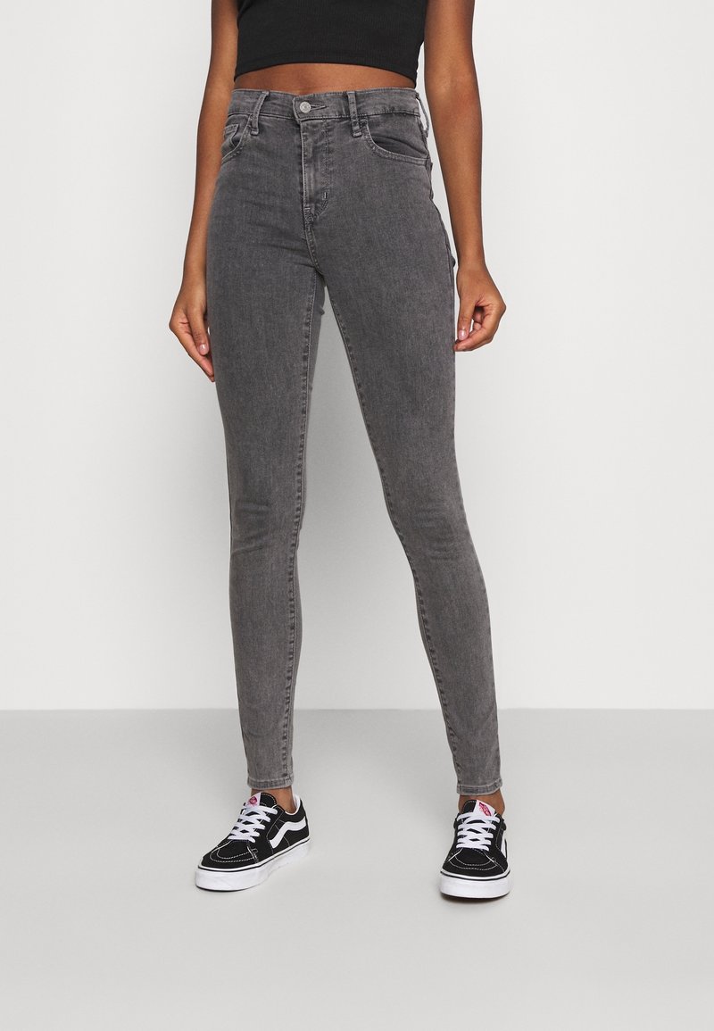 Grå tight jeans med fem fickor, hög midja och en subtil blekt textur, kombinerat med svartvita sneakers.