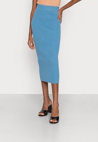 Žebrovaná tužková sukně v světle modré barvě, po kolena, s vysokým pasem. V kombinaci s černými lodičkami s otevřenou špičkou. Pozadí na rovné ploše.