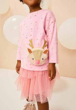 Kind, der ein pinkfarbenes Oberteil mit Sternmuster, einen pinken, mehrlagigen Tüllrock, eine beige Rentierbörse und beige Stiefel mit weißen Lace-Socken trägt.