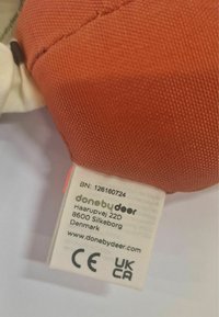 Kangasilt, mis on valmistatud oranži puuvillast kangast, millel on valgest puuvillast etikett. Etiketil on brändi nimi, asukoht ja vastavusmargid.