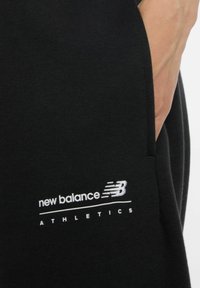 Sweatshirt noir avec une texture douce et une coupe droite, comportant un logo "new balance" brodé en blanc et le texte "ATHLETICS" en dessous.