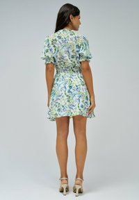 Vestido corto floral en verde y azul, con mangas abullonadas, cintura fruncida y falda acampanada. Combinado con sandalias de tacón altas en color beige.