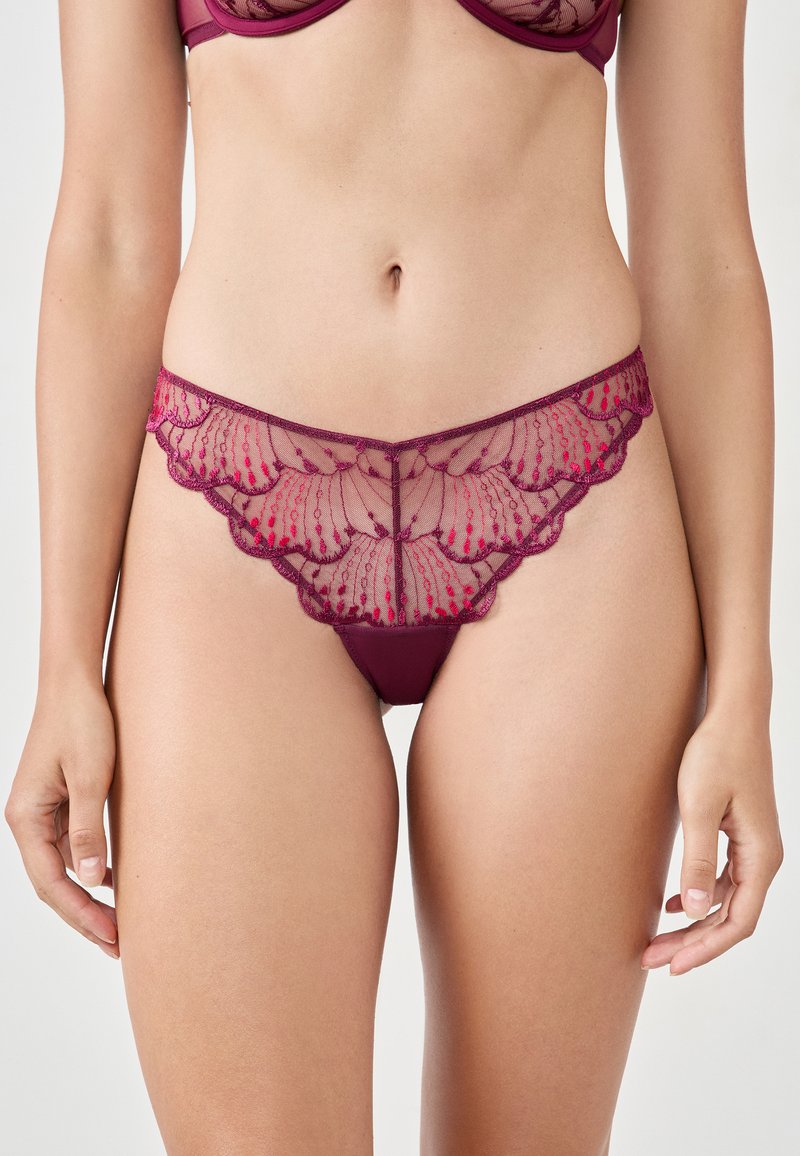 Lingerie en dentelle bordeaux avec un design à volants, panneaux transparents ornés de motifs floraux complexes et une ceinture en tissu lisse.
