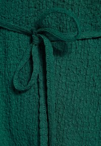 Textured green fabric with a crinkled appearance, featuring a tied belt detail. The material is lightweight and drapes softly.