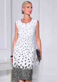 Weißes ärmelloses Kleid mit schwarzen Blumenmustern, ausgestattet mit einem V-Ausschnitt und einem schwarzen, verzierten Saum. Zubehör nicht enthalten.