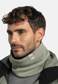 Gaiter de cuello de punto verde claro hecho de material suave, con una etiqueta de logo. Llevado de manera casual alrededor del cuello, debajo de una chaqueta.