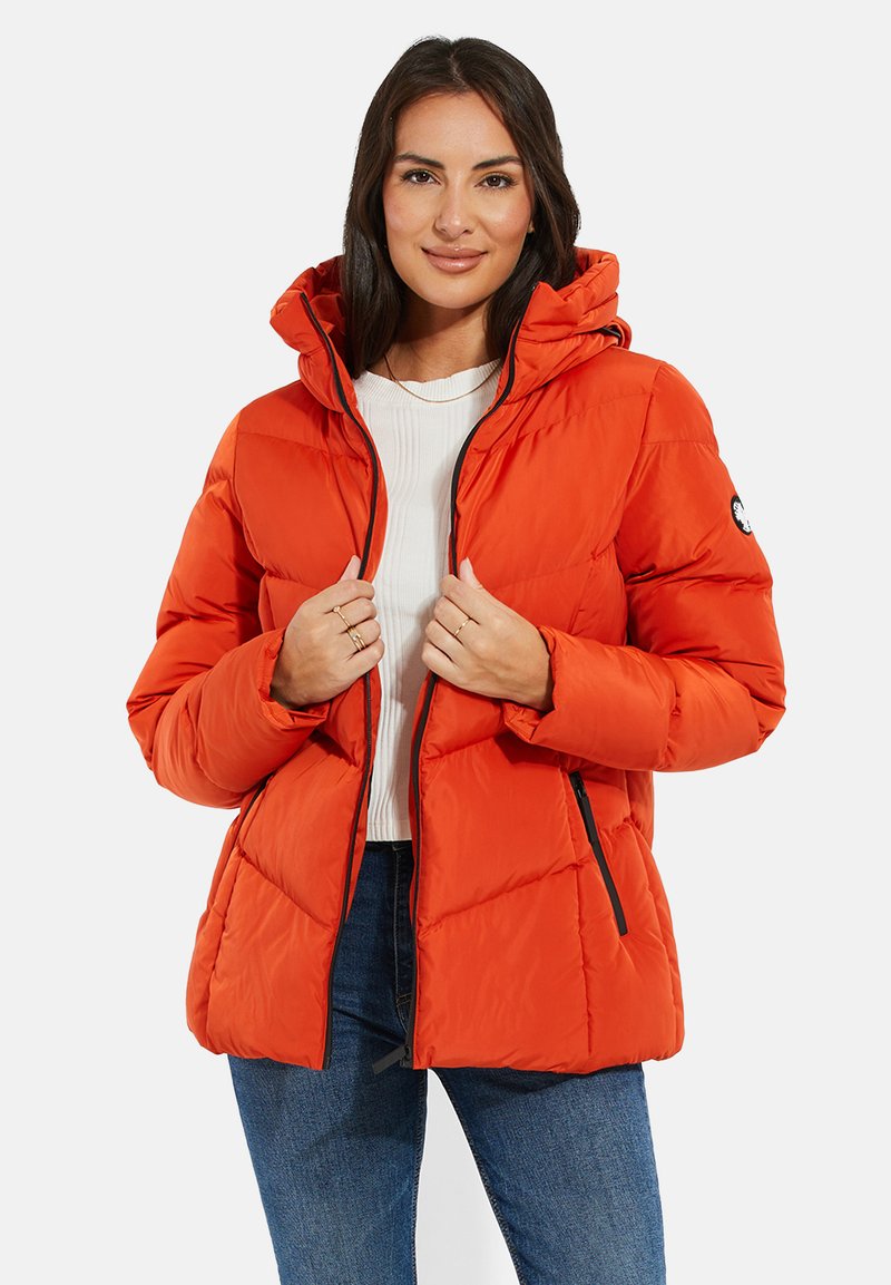 Doudoune orange vif avec capuche, présentant un design matelassé, des accents de fermeture éclair noirs et des poches latérales, portée sur un haut blanc.