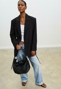 Schwarzes Blazer mit einem Knopf, kombiniert mit einem weißen Tanktop und hellblauen weit geschnittenen Jeans. Schwarze Leder-Hobo-Tasche, flache Sandalen.