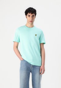 T-shirt en coton vert menthe à manches courtes et col rond, avec un petit logo de papillon jaune sur la poitrine gauche.