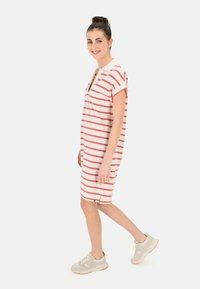 Gestreiftes Kurzarmkleid in Creme mit roten Streifen, mit V-Ausschnitt, lockerer Passform, Seitenschlitzen und einem lässigen Stil. Kombiniert mit leichten Sneakern.