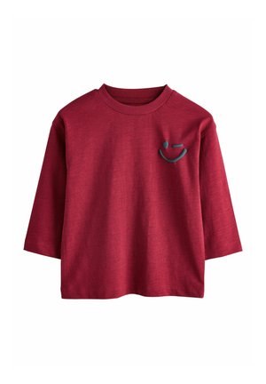 Rotes, geripptes Langarmshirt mit einem Rundhalsausschnitt und einem blauen Smiley-Gesicht-Design auf der linken Brust. Weicher Stoff, lockere Passform.