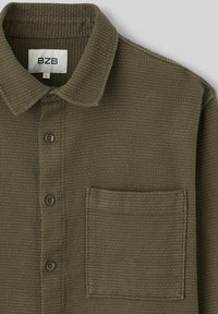 Chemise à col vert olive en tissu texturé, dotée d'une poche plaquée, d'une fermeture à boutons et de cinq boutons assortis.