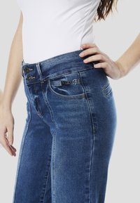 Donkerblauwe denim jeans met een hoge taille, voorzien van twee zwarte knopen, zijzakken en licht vervaagde delen langs de voorste naden.