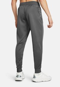 Pantalones deportivos grises de tela suave, con cintura elástica, ajuste ceñido y puños acanalados en los tobillos. Dos bolsillos laterales visibles.