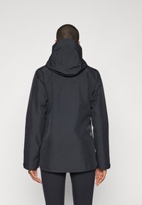 Black waterproof jacket with a hood, featuring a simple design, long sleeves, and a slightly curved hem at the back. Smooth texture.