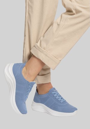 Person wearing light blue knit sneakers with white soles and beige corduroy pants against a gray background.