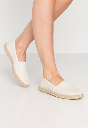 Beige slip-on sko lavet af tekstureret stof med en flad jute-sål. Har et enkelt design uden synligt hardware eller accenter.