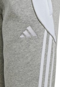 Graue Baumwoll-Jogginghose mit weißen Seitenpaneelen und drei weißen Streifen. Verfügt über ein gesticktes graues Adidas-Logo im oberen Oberschenkelbereich.