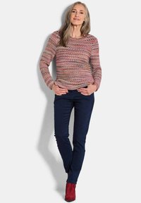 Maglione lavorato a maglia con motivo multicolore, scollatura rotonda, maniche lunghe. Abbinato a pantaloni blu scuro e stivaletti rossi alla caviglia. Texture complessivamente liscia.