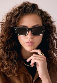 Schwarze Katzenaugen-Sonnenbrille mit durchscheinend braunen Schildpattdetails an den Rändern. Glänzende Oberfläche, mit großen dunklen Gläsern.