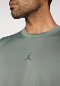 Αθλητικό μπλουζάκι σε ανοιχτό πράσινο χρώμα με στρογγυλή λαιμόκοψη και μαύρο λογότυπο Jumpman στο στήθος, με ομαλή, υφασμάτινη υφή.