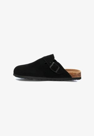 Zueco de ante negro con punta redondeada y hebilla lateral. Plantilla de corcho y suela de goma, con una textura suave y mate.