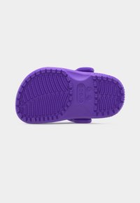 Σόλα μοβ παπουτσιού Crocs, που δείχνει τα σχέδια πέλματος και τις ενδείξεις μεγέθους σε απλό ανοιχτό φόντο.