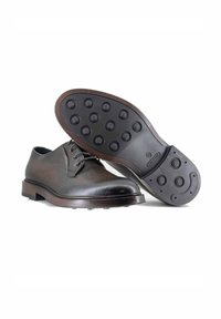 Scarpe in pelle marrone con punta arrotondata, dotate di un design con lacci e una suola in gomma testurizzata con punti di presa circolari.