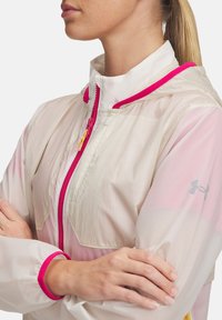 Leichte, semi-transparente Jacke in Off-White mit rosa Akzenten. Sie hat einen hohen Kragen, einen durchgehenden Reißverschluss und elastische Bündchen. Logo am Ärmel.