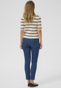 Lichtgewicht gestreepte top in crèmekleur en marineblauw, gecombineerd met donkerblauwe skinny jeans. De top heeft korte mouwen en een getailleerd ontwerp.