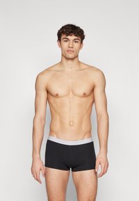 Sorte boxer briefs med en lys grå linning, laget av mykt stoff, som har en tettsittende passform og glatt tekstur. Modellen står oppreist.