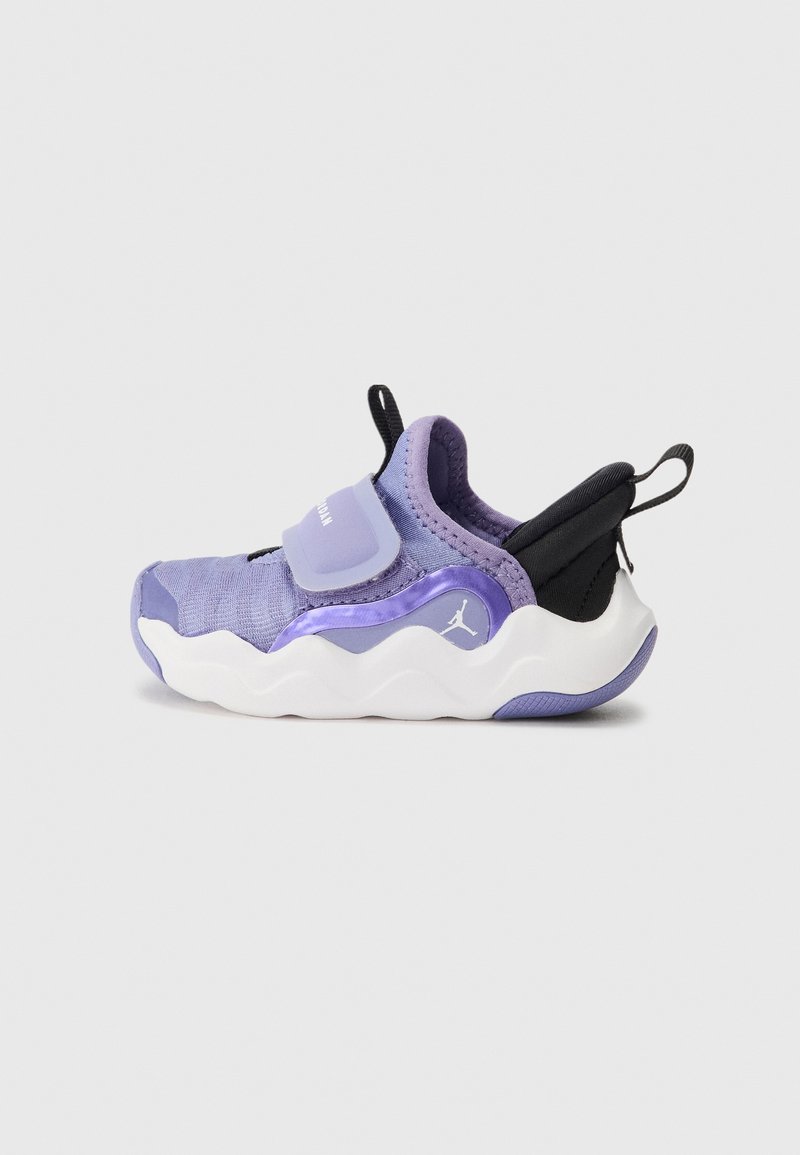 Zapatilla morada y negra con un upper de tejido texturizado, una correa de velcro y una suela blanca ondulada. Presenta un logo de marca en el lateral.