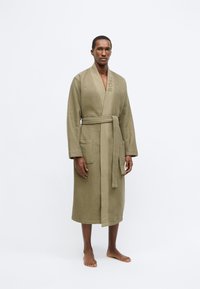 Accappatoio verde oliva con trama a nido d'ape, cintura abbinata, tasche laterali e logo "BOSS" tonale sul colletto, design fino al ginocchio.