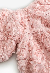 Light pink fabric densely covered with small, overlapping petal-shaped appliques creating a textured, floral-like surface.
