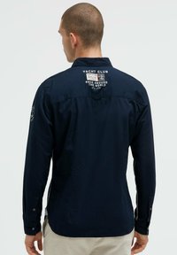 Marineblaue Langarmbluse mit bestickten Aufnähern, Knopfmanschette und Kragen, aus glattem Stoff mit lockerem Schnitt.