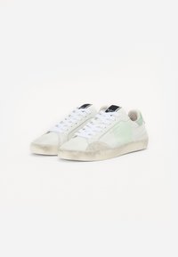 Sneakers con una toma in pelle bianca, accenti verde chiaro, puntale beige testurizzato e lacci bianchi con un logo nero sulla linguetta.