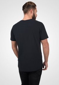 Camiseta de manga corta negra con dobladillo redondeado. Hecha de algodón suave, presenta un diseño simple sin patrones ni acentos visibles.