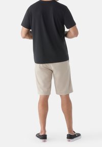 Camiseta negra de manga corta, pantalones cortos beige y zapatos negros tipo slip-on. Tejido de algodón suave, corte relajado y diseño sencillo sin patrones visibles.