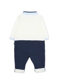 Salopette en coton avec un haut blanc et un bas bleu marine. Comprend des accents bleu clair sur les poignets et le col. Inclut des poignets retroussés et une étiquette sur le côté.